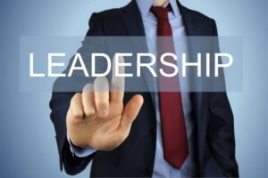 Businessperson in a dark suit extending a finger forward with the word LEADERSHIP overlay.